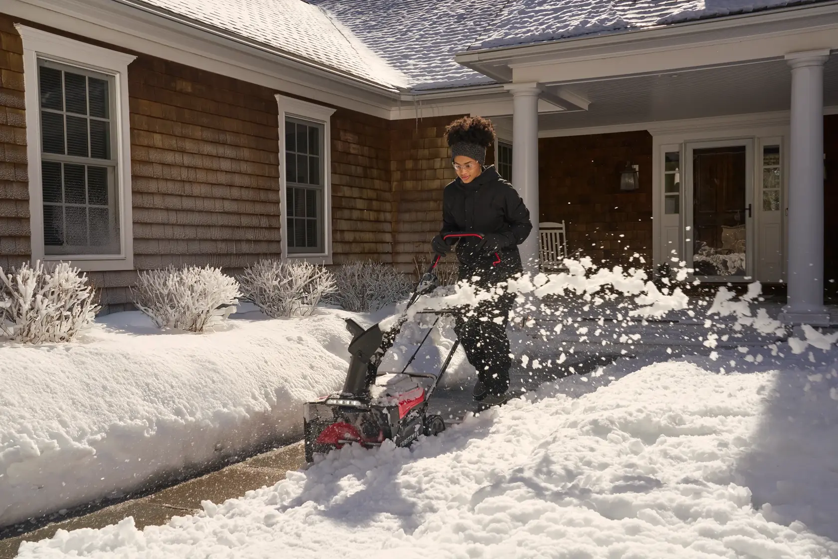 Woman clearing sidewalk path with snow shooting wide angle with CRAFTSMAN 2x20V 18" Snow Blower