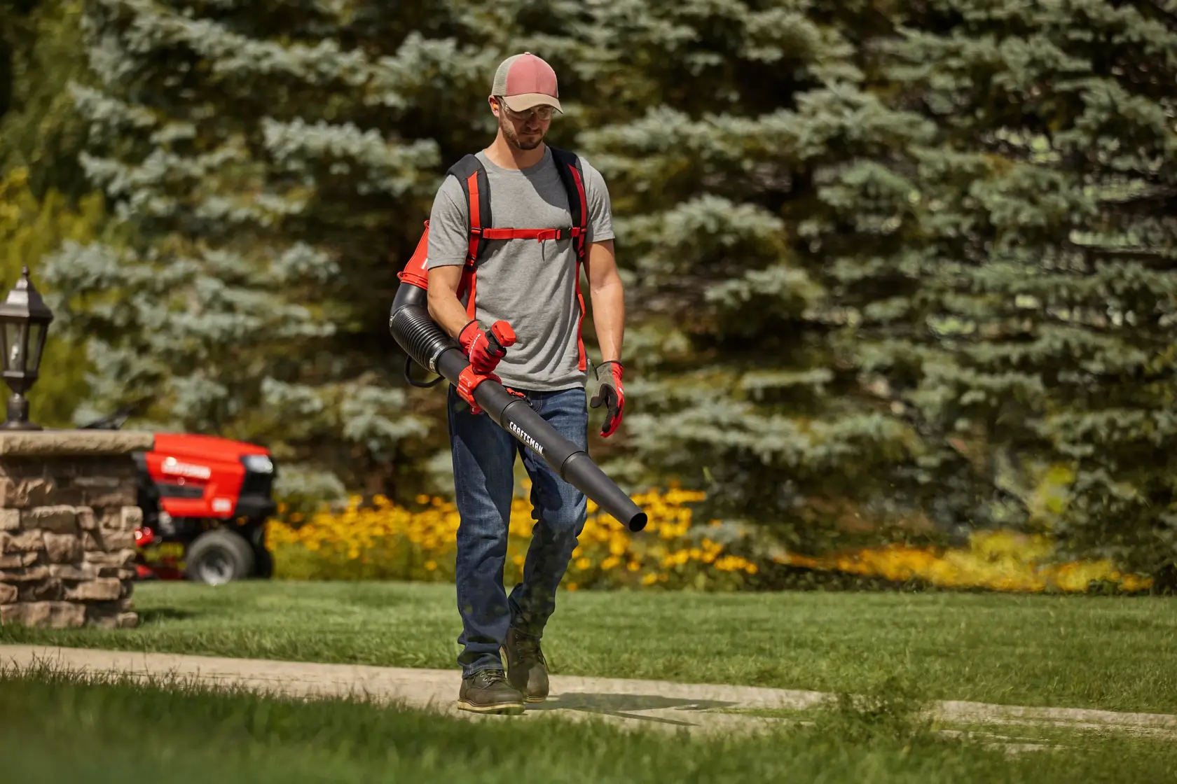 Photo d'une personne utilisant le souffleur à dos CRAFTSMAN CM41AR51BP593 sur un trottoir dans un jardin avec des arbres en arrière-plan.