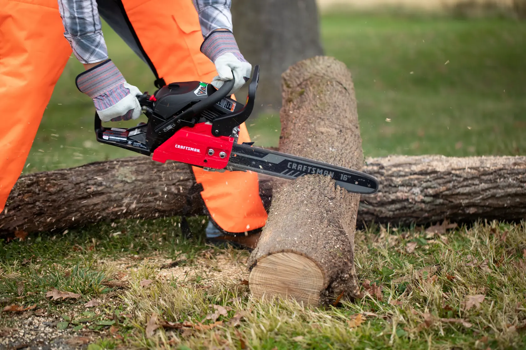Photo of CRAFTSMAN chainsaw SKU CM41AY4216593 cutting a log outdoors, worker in orange pants and gloves holding saw.