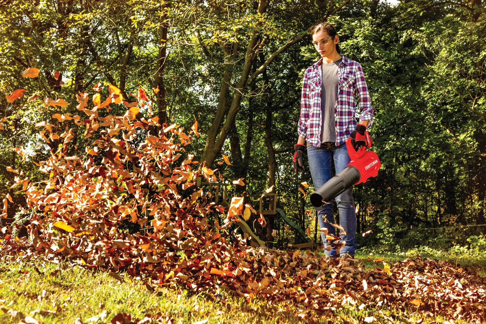 Brushless cordless axial blower kit 4 amp hour being used for cleaning dead leaves from lawn by person.