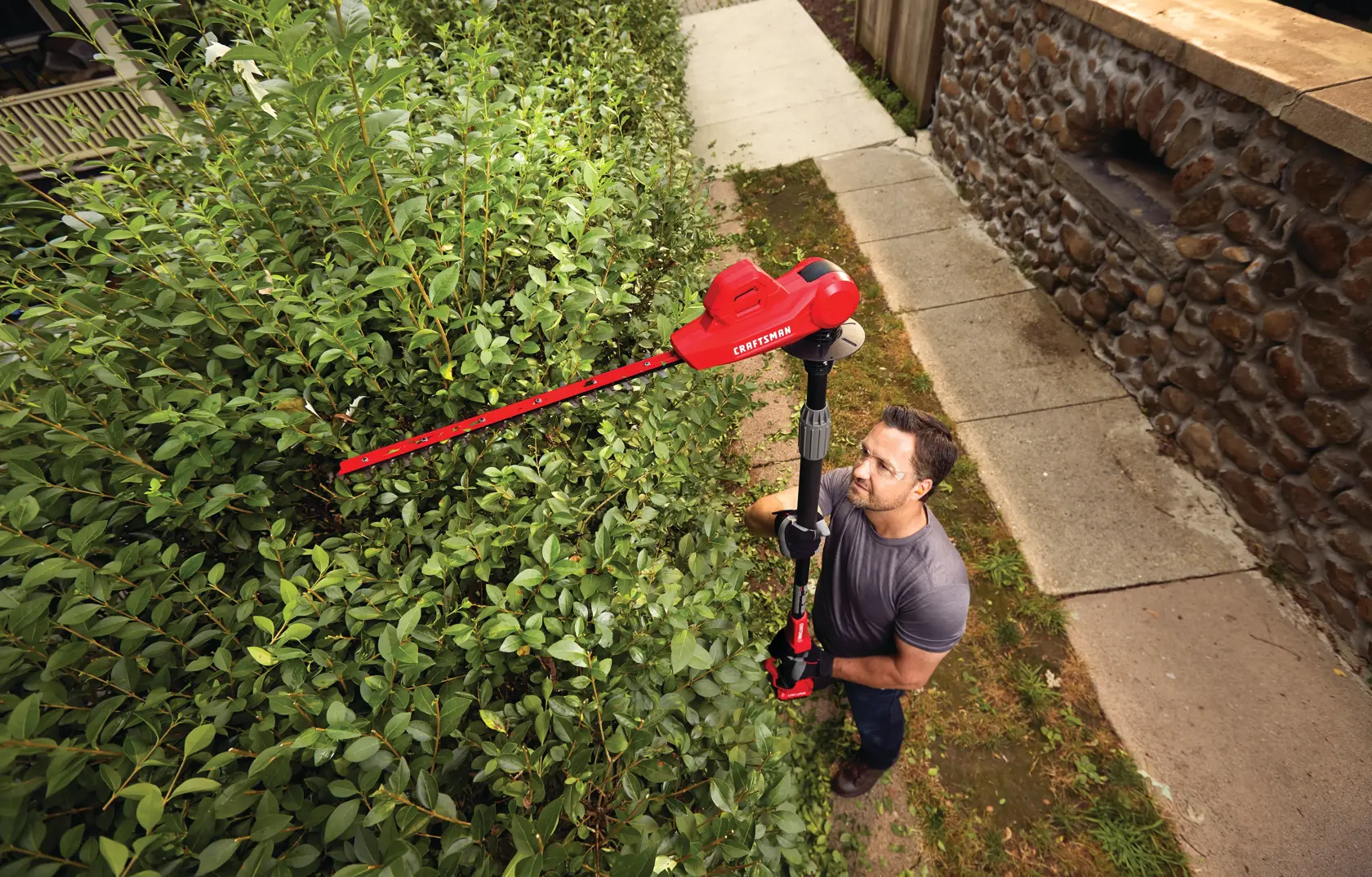 20 volt 18 inch cordless pole hedge trimmer kit being used by a person to trim plants.