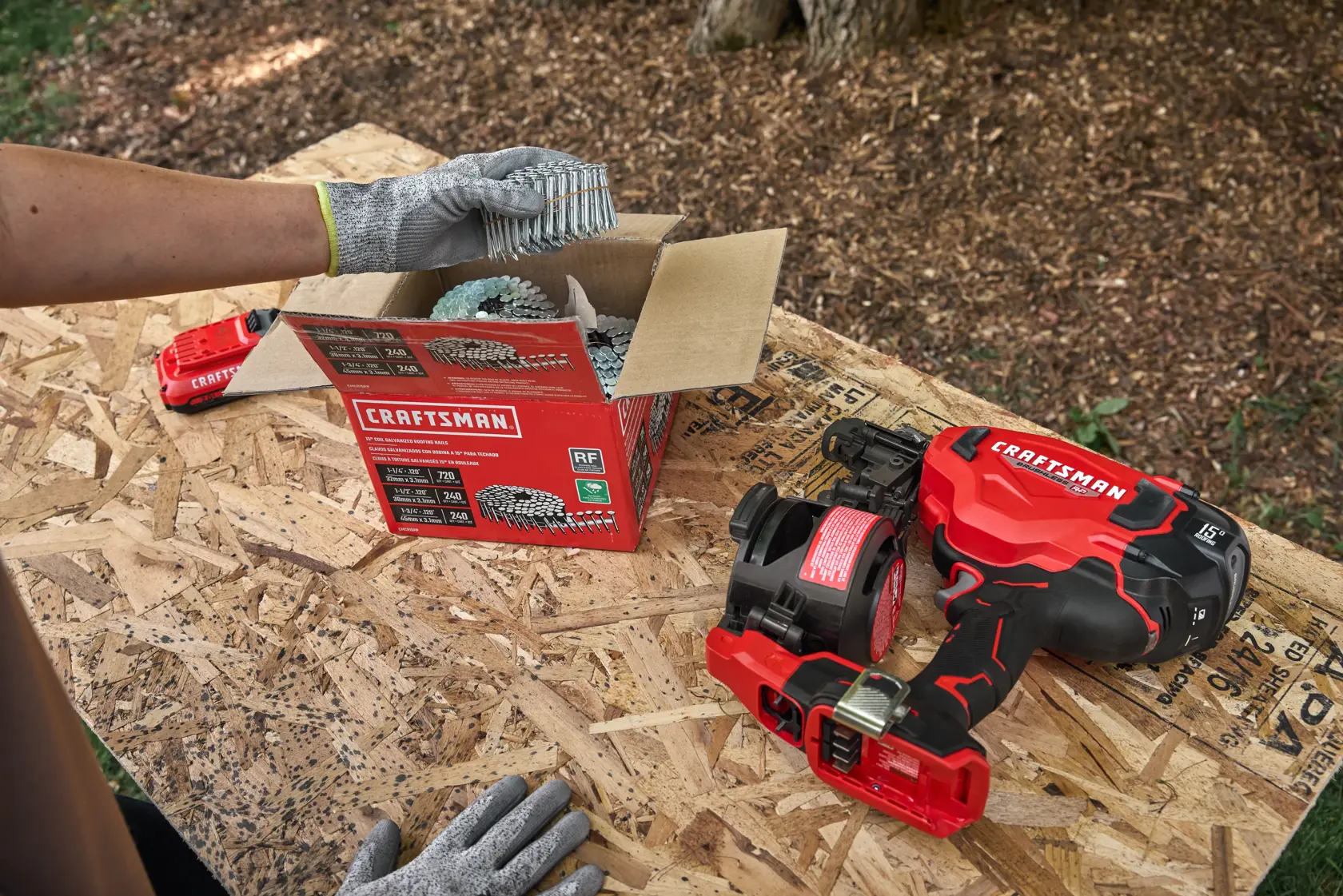 Gros plan sur un espace de travail de menuiserie avec une boîte de clous en rouleau CRAFTSMAN, une batterie et un pistolet à