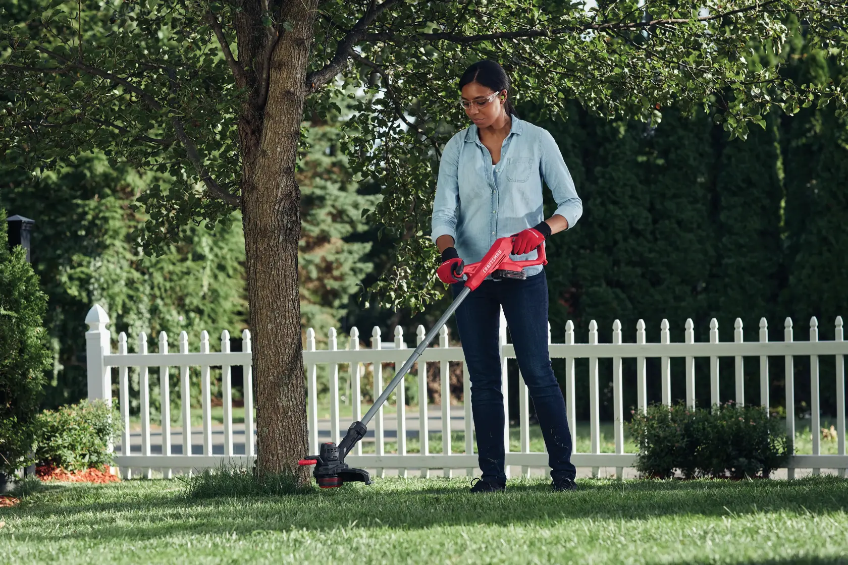 Woman using the CRAFTSMAN V20 Cordless 10 inch Weedwacker String Trimmer and Edger to trim around a tree