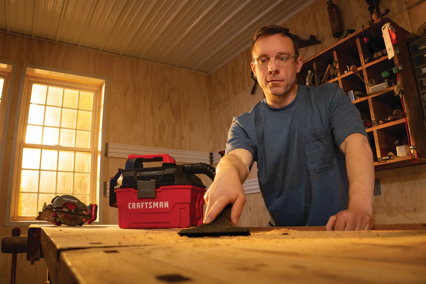 20 volt cordless 2 gallon wet dry vacuum being used by a person to clean wooden work station.