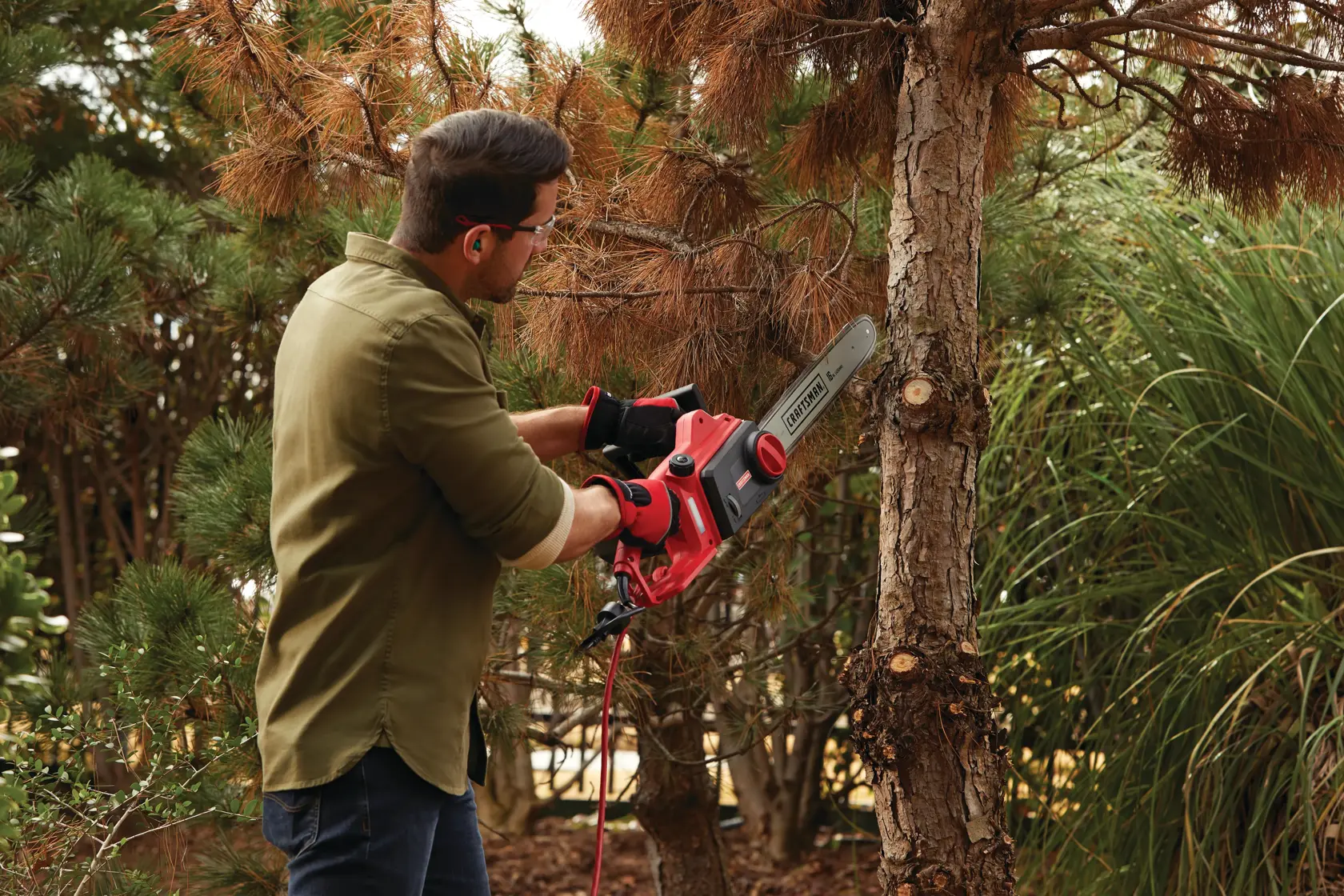 Photo of Craftsman CMECS600 electric chainsaw used outdoors to cut tree branches, brand name visible.