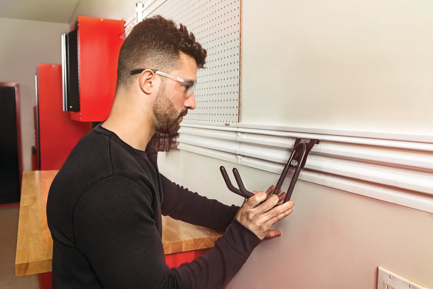 Photo of a person installing a CRAFTSMAN wall storage hook, SKU CMST23201RB, on a white garage track system.