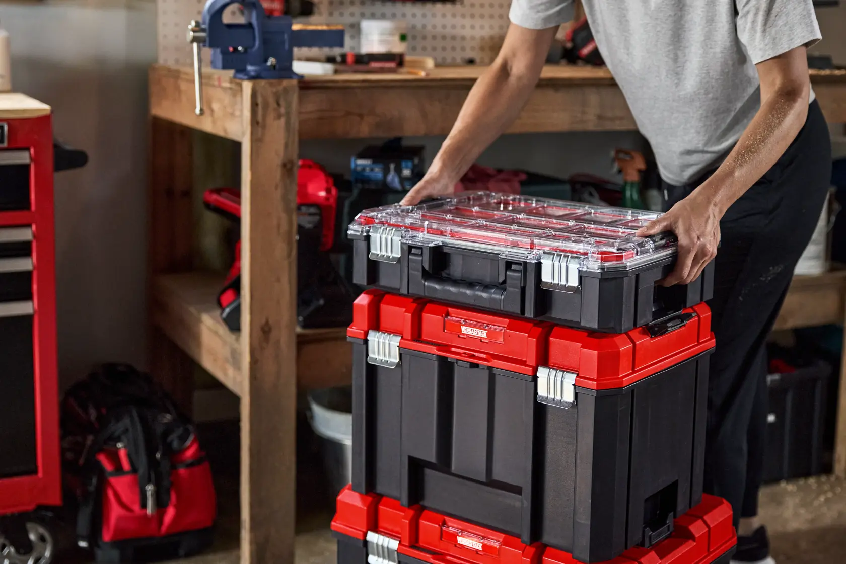 Photo of CRAFTSMAN modular black and red stackable tool boxes, SKU CMST60402, on a workshop floor with a person organizing them.